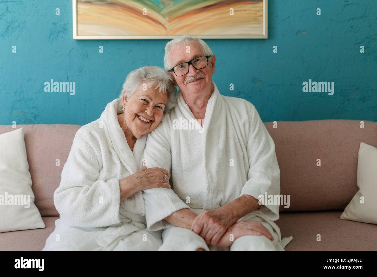 Happy senior couple sitting together in bathrobe on sofa, having nice time at home. Stock Photo