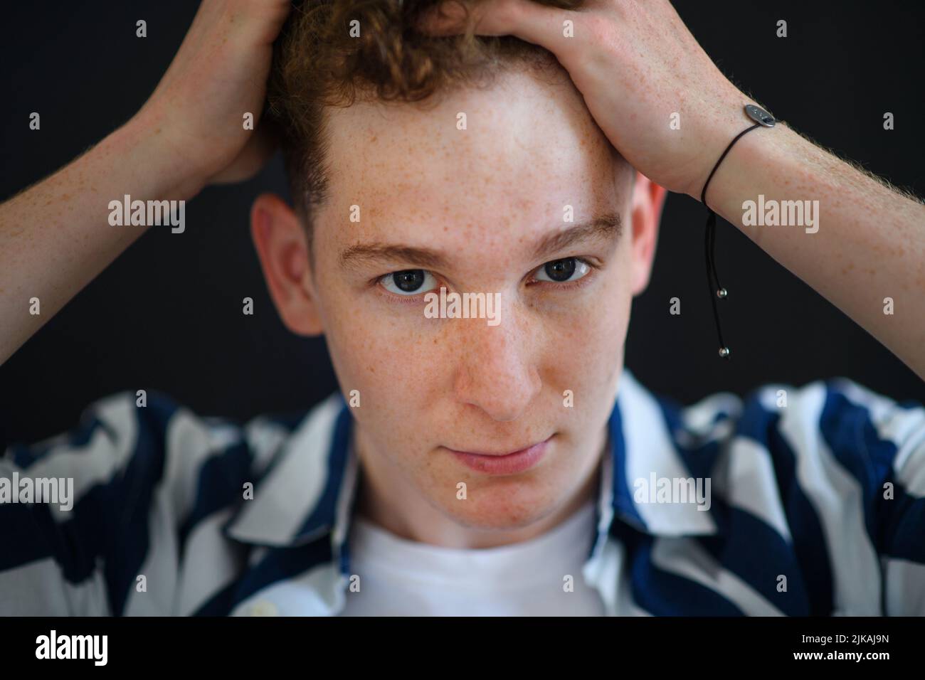 Portrait of thoughtful handsome young man with ginger hair and freckles looking away on black background, close-up Stock Photo