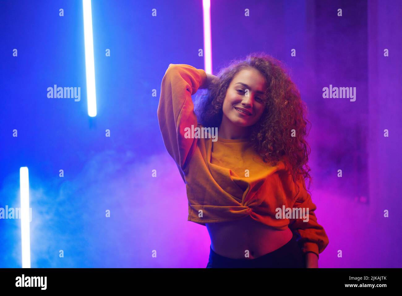 Portrait of a happy young woman dancing over neon light background at disco party Stock Photo