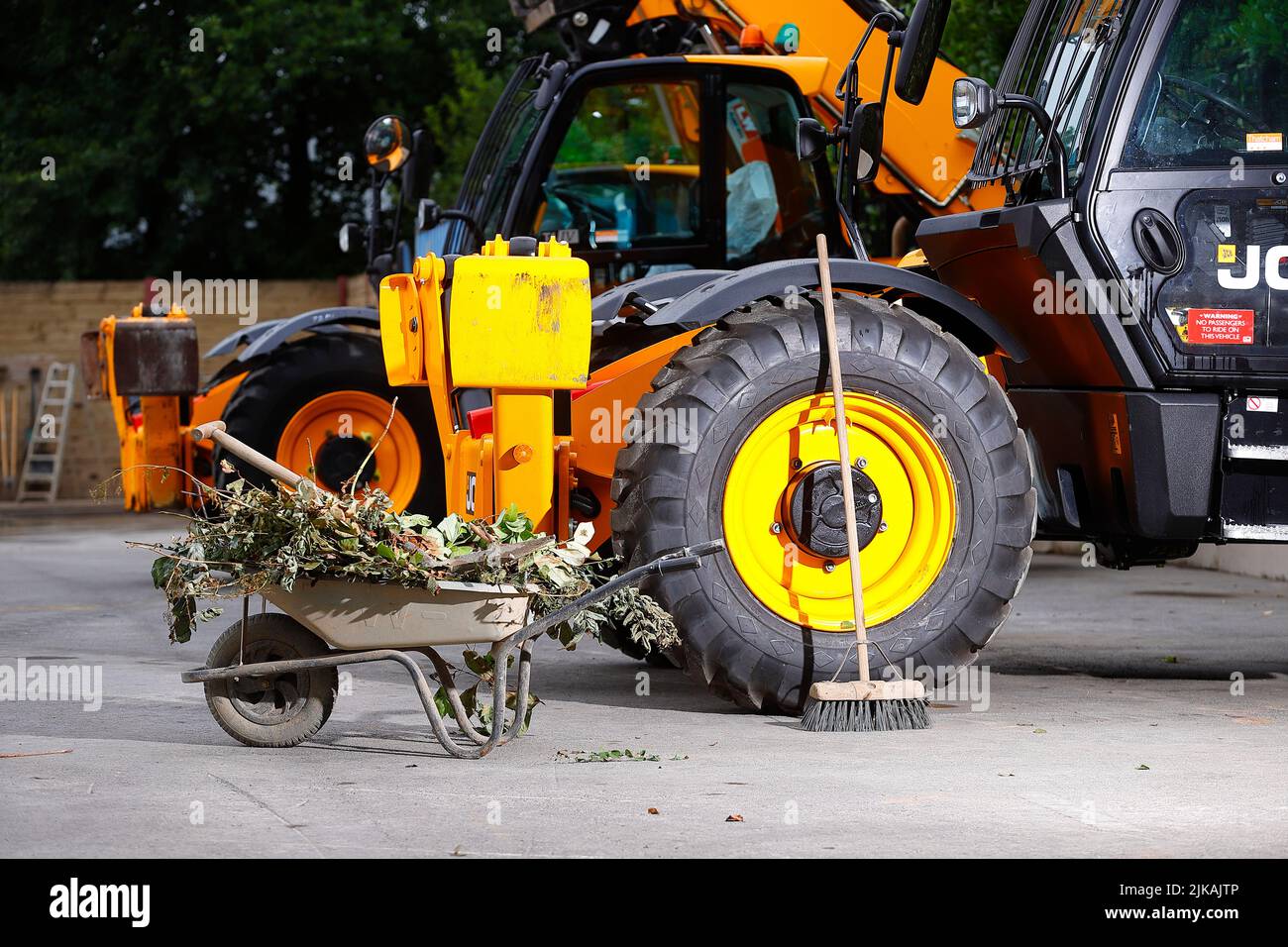 A wheelbarrow and brush pictured with JCB Telehandlers at a plant hire yard Stock Photo