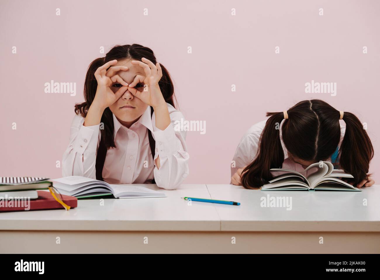 Studying dry dull subject. Schoolgirl twins, sitting behind the desk bored Stock Photo
