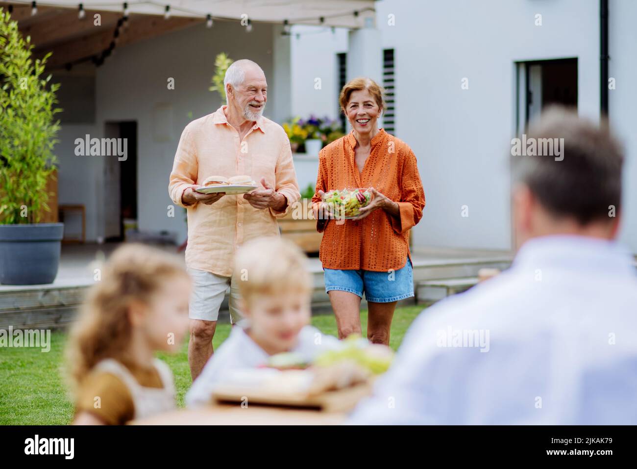 Happy senior couple bringing salad and burgers at multi generation garden party in summer. Stock Photo