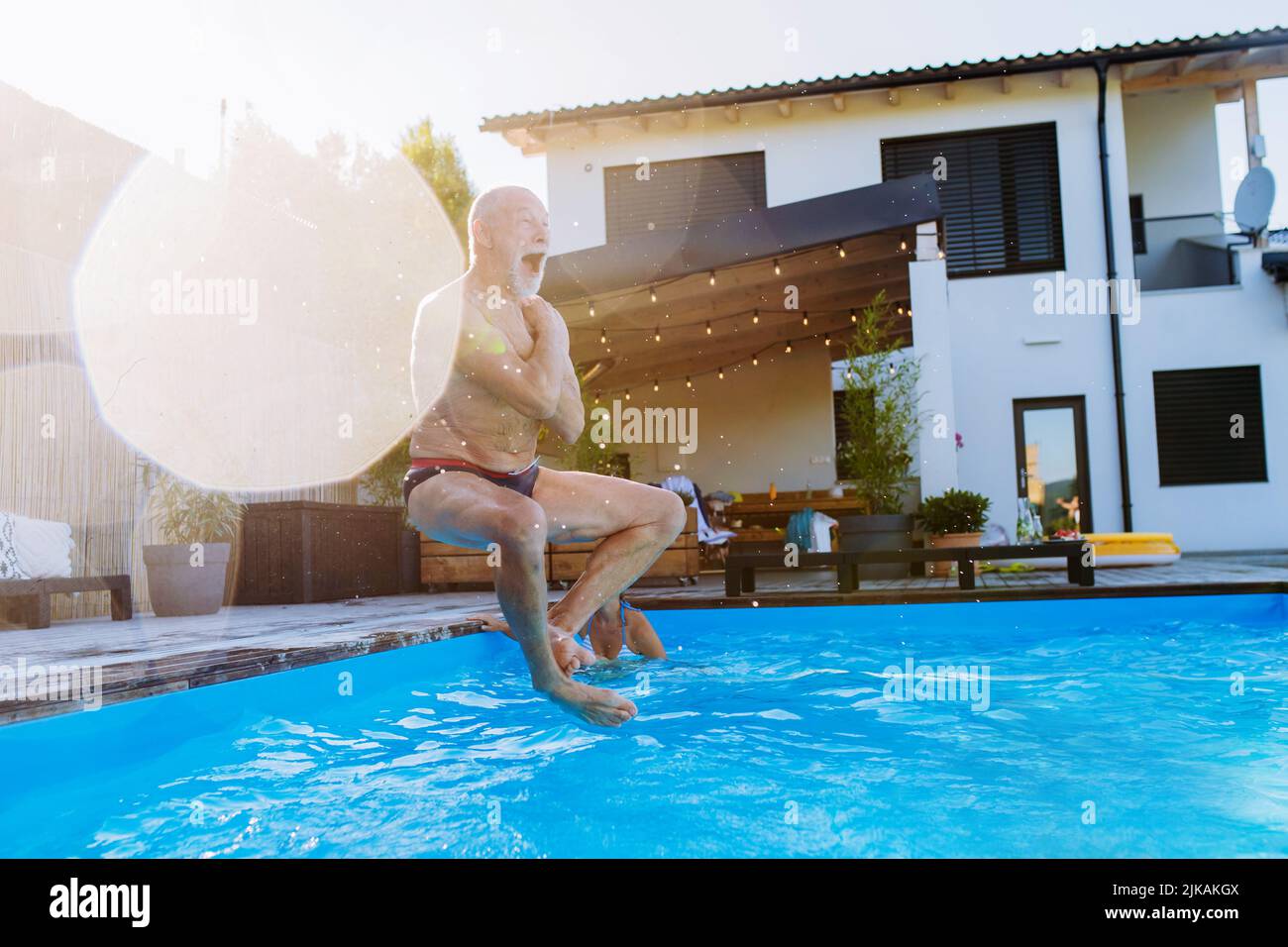 Happy senior man jumping into the swimming pool at backyard. Stock Photo