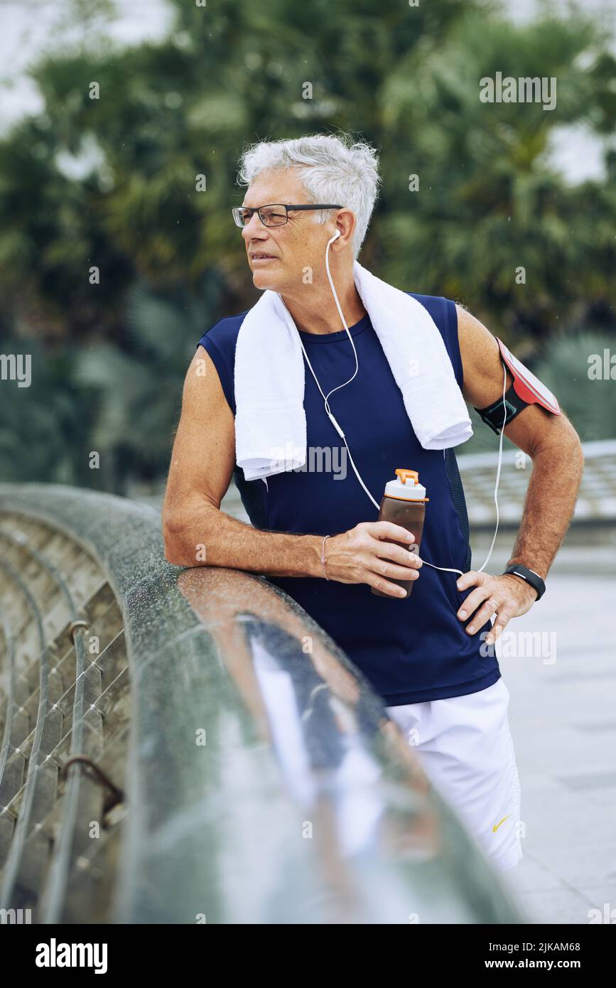 Elderly man drinking water after jogging in the morning Stock Photo