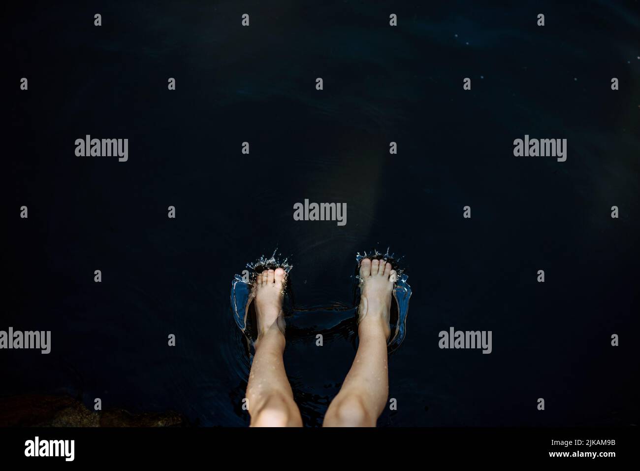 Close-up of kids legs relaxing in lake during hot summer day, top view. Stock Photo