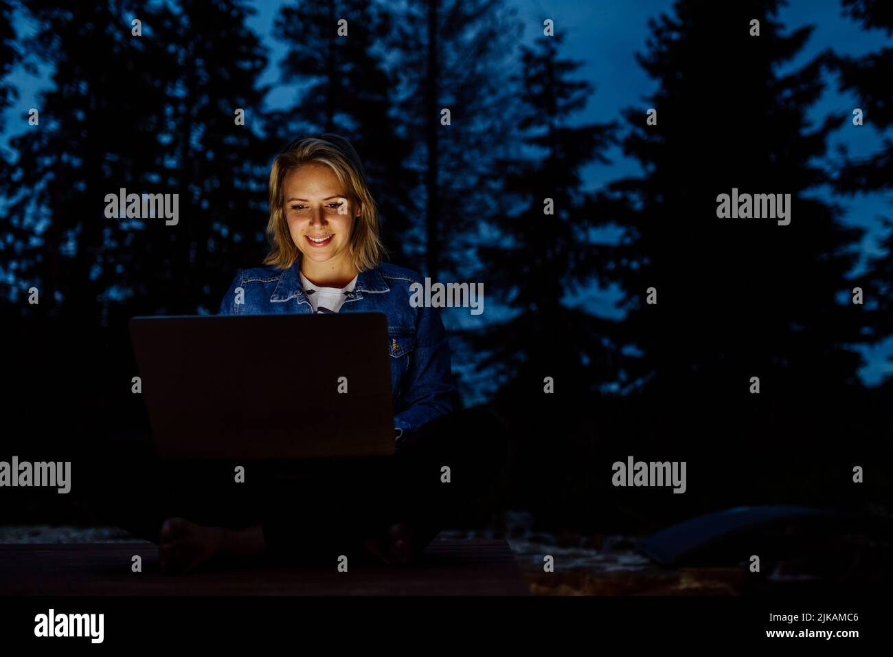 Woman, freelancer working on laptop, sitting outdoor in the evening, concept of remote office, work during vacation. Stock Photo