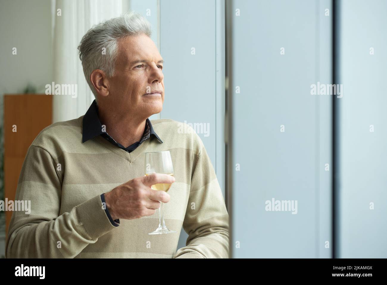 Pensive aged man looking through the window and drinking wine Stock Photo