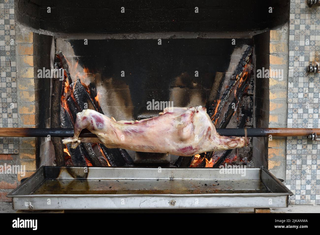 The carcass of a young sheep roasting on a spit over a low fire in oven. Roasted lamb on a spit. Kitchen in the open air. Local cuisine in Dagestan. R Stock Photo