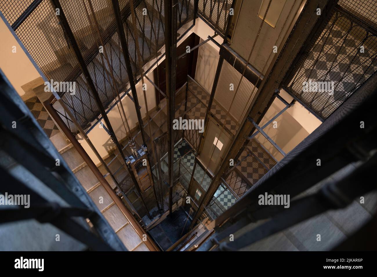 Dramatic shot of a stairwell looking into an elevator shaft with metal rods, cables and cabin in a vintage apartment building in Rome Stock Photo