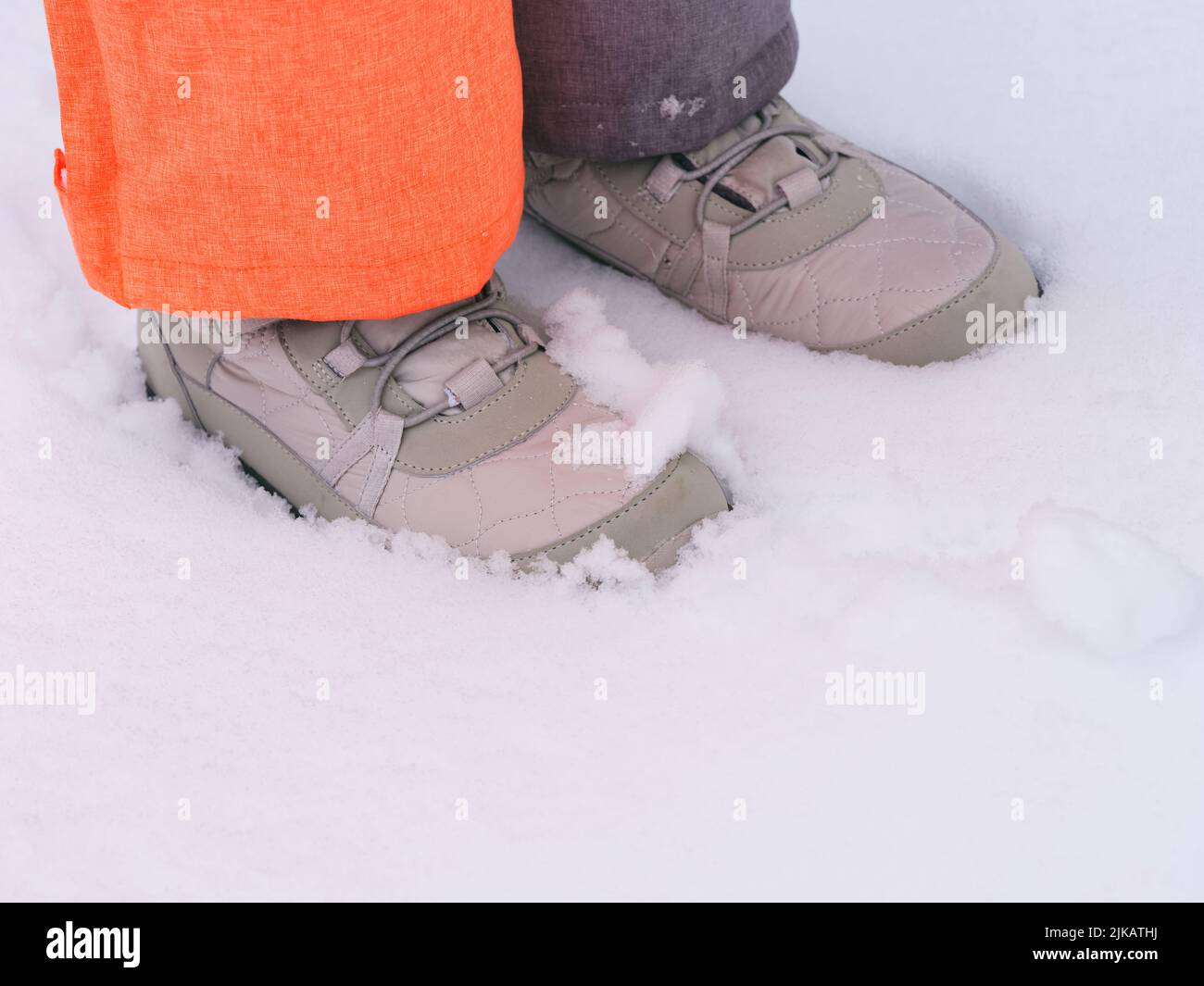 A close-up shot of child feet in winter shoes standing on snow. Stock Photo
