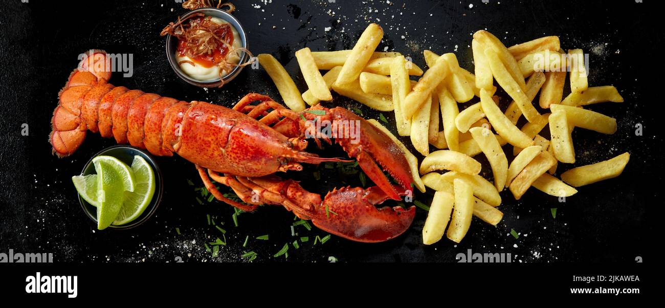 Top view of delicious lobster and heap of potato chips placed on black background near fresh lime pieces and bowl on sauce Stock Photo