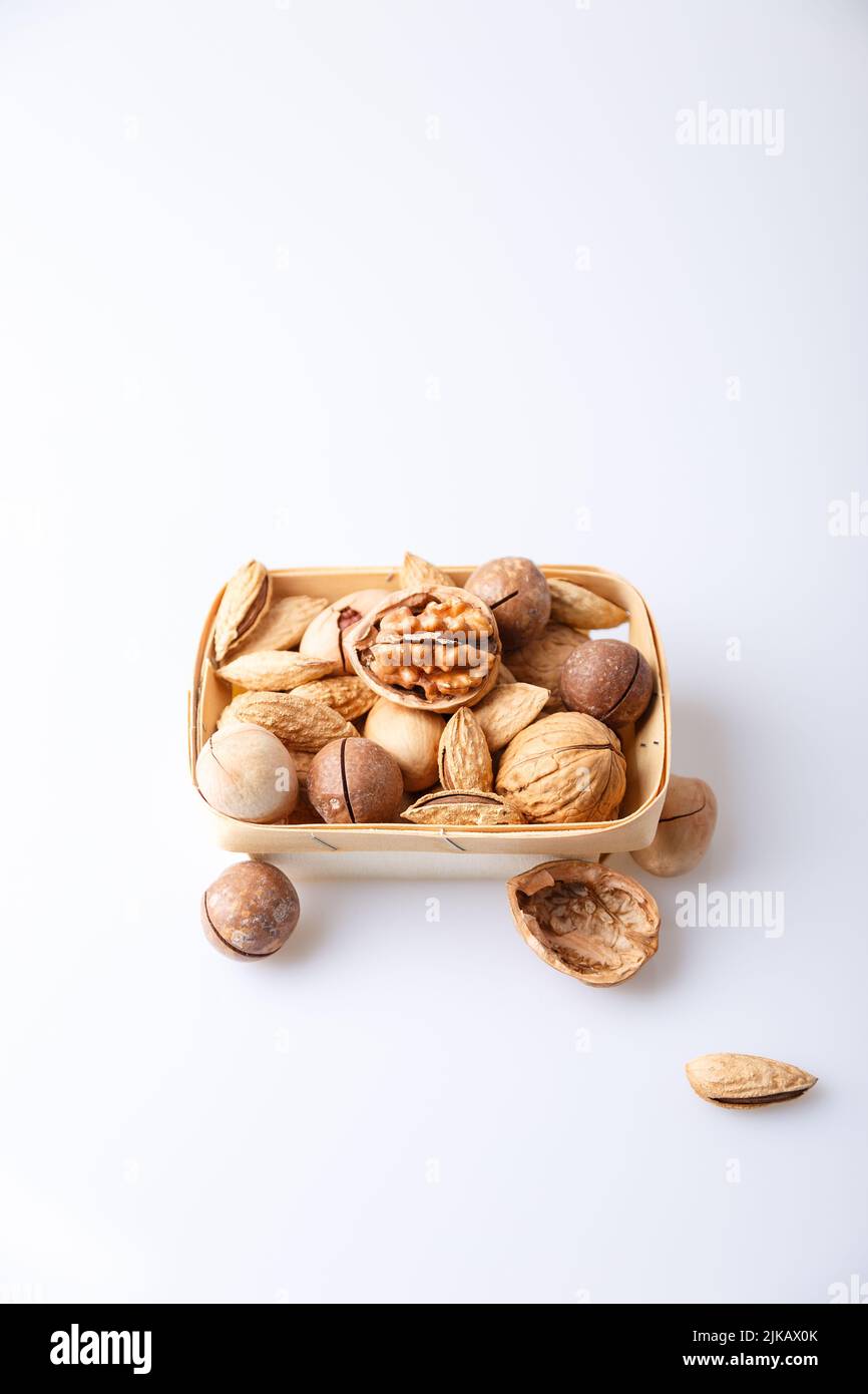 Assorted nuts in the shell on a white background: walnuts, pecans, almonds, macadamia. Nuts in a basket. Selective focus, close-up. Place for text. Stock Photo