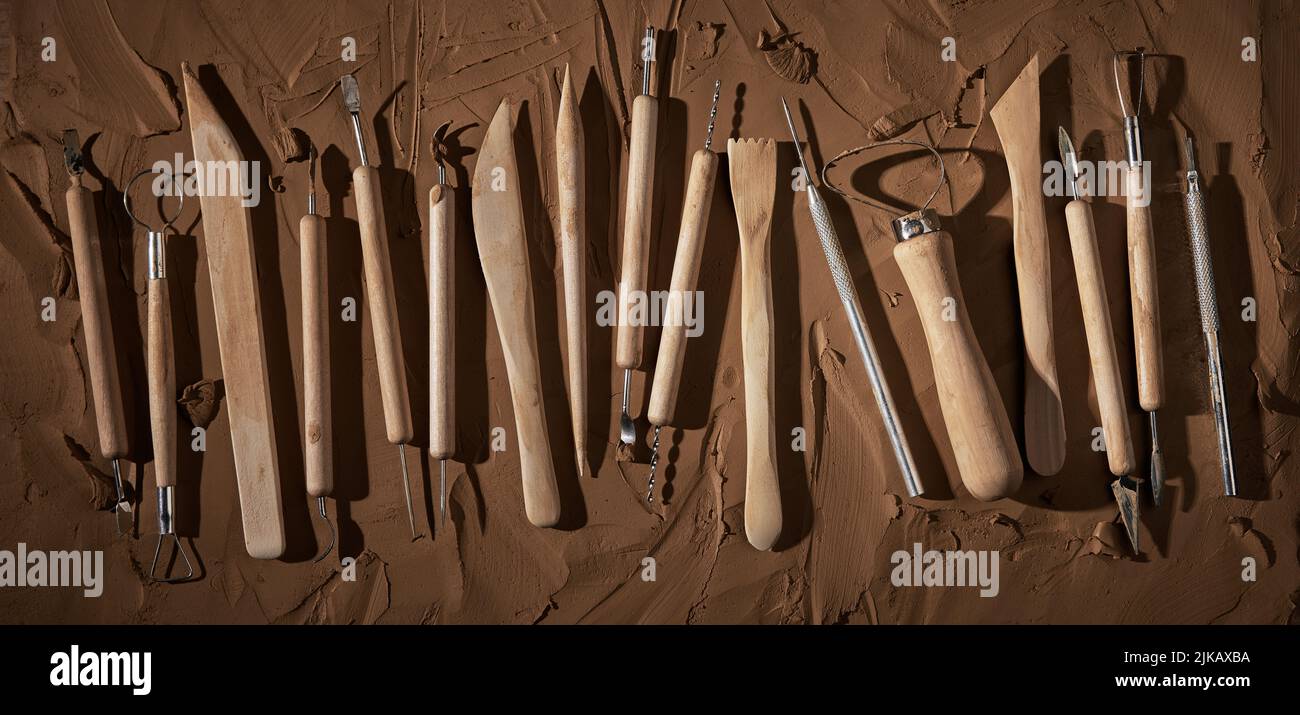 Top view of various instruments with wooden handles for carving and sculpturing clay placed on brown background in light professional workshop Stock Photo