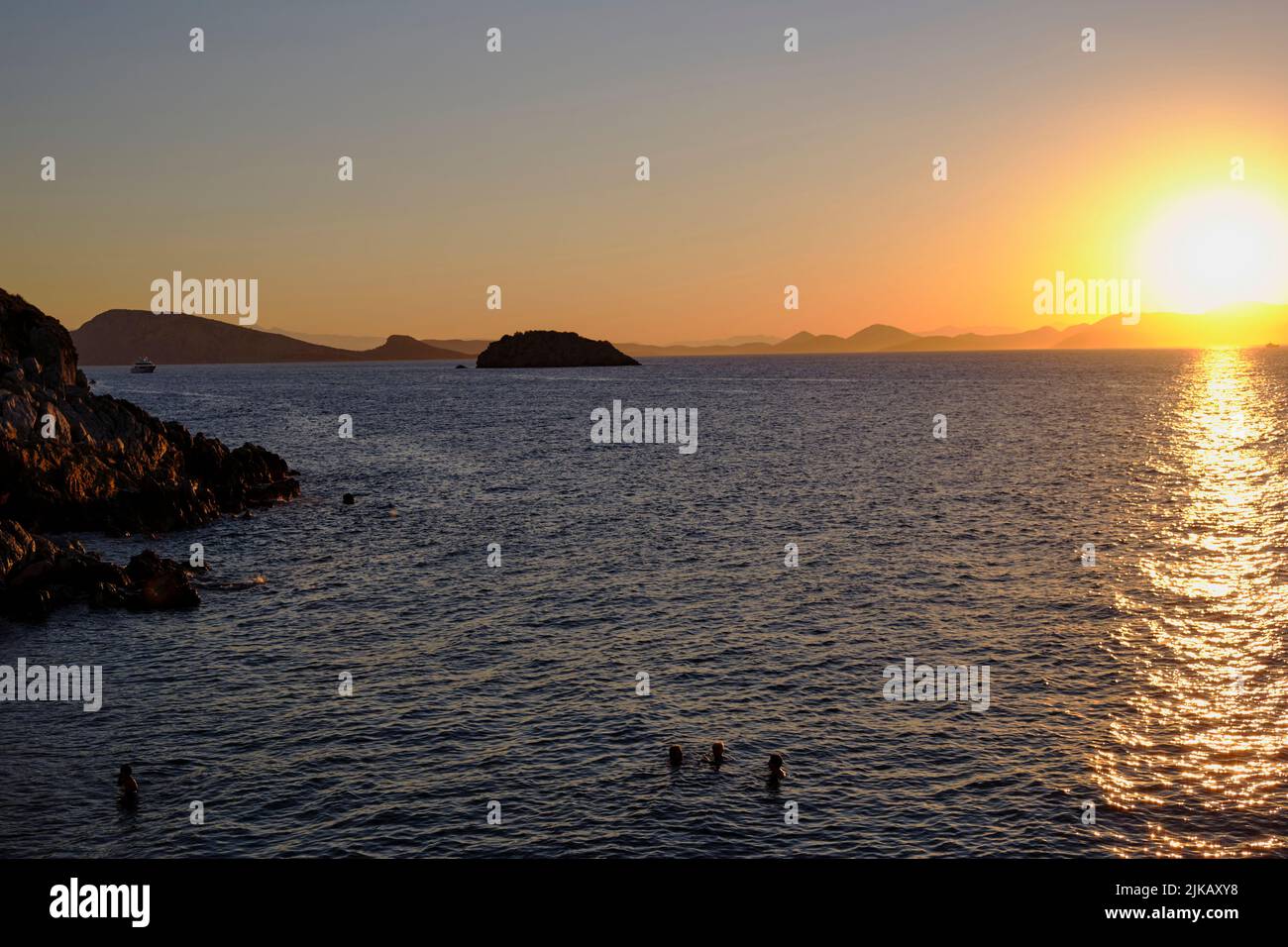 tourists swimming at sunset on the island of Hydra in Greece in Summer Stock Photo