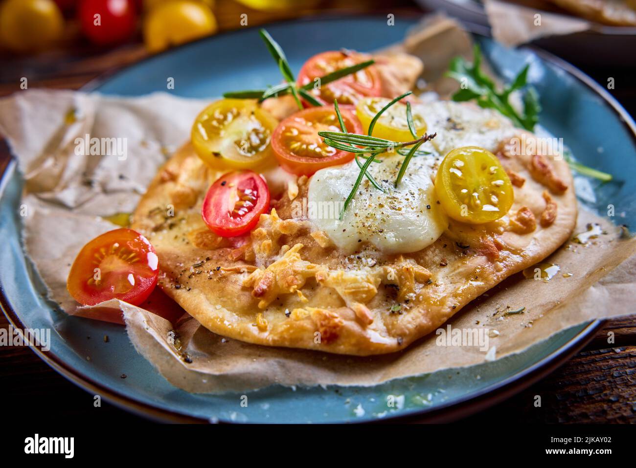 From above of appetizing flatbread pizza with red and yellow cherry tomatoes mozzarella cheese and herbs topped with olive oil and served on plate in Stock Photo