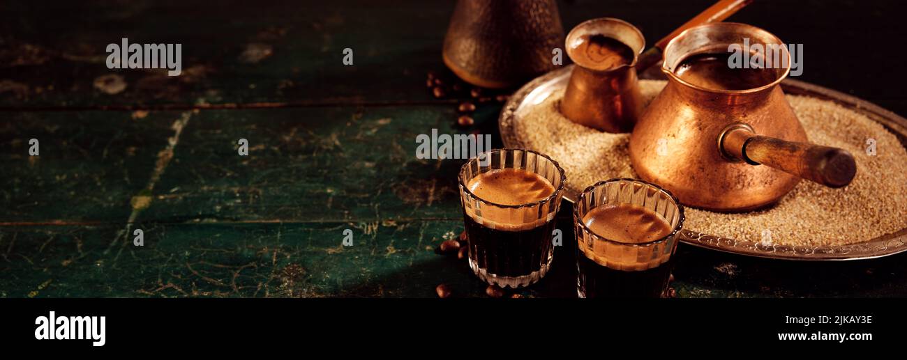 Metal cezves on tray with sand and glasses filled with hot aromatic oriental coffee served on shabby table in kitchen Stock Photo