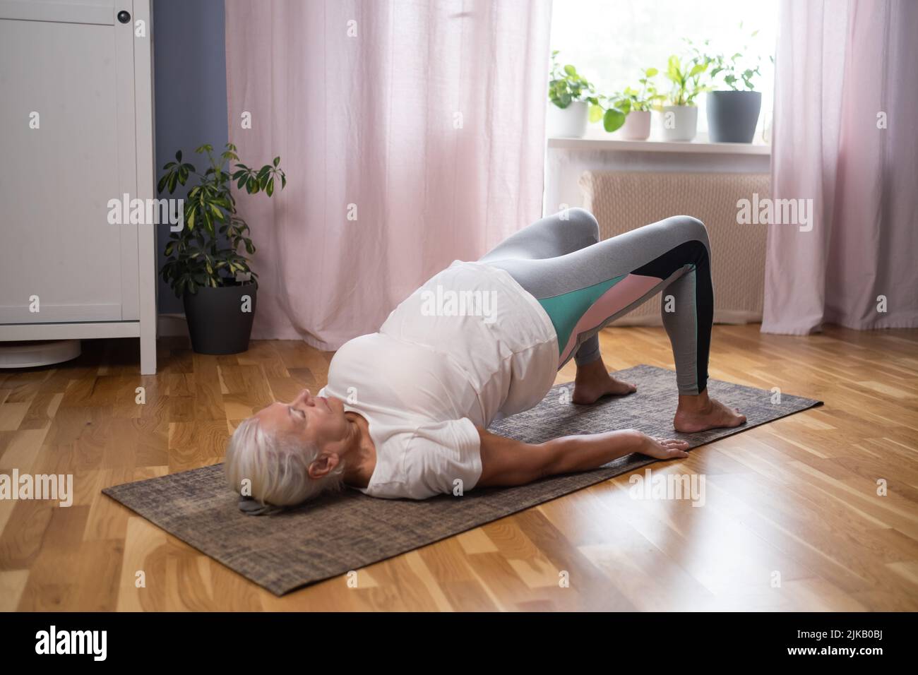 Senior athletic yoga woman doing ardha chakrasana wheel on yoga mat at home Stock Photo