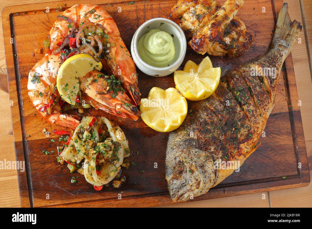 Mixed seafood platter with tiger prawns, calamari and whole grilled fish garnished with lemon and sauce Stock Photo