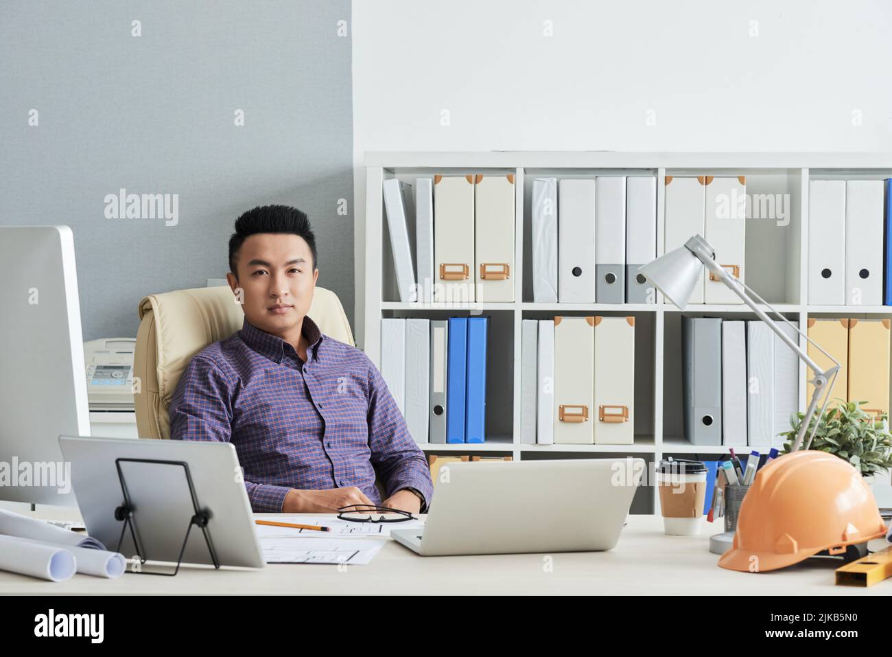 Confident young Vietnamese engineer sitting at his table in office Stock Photo