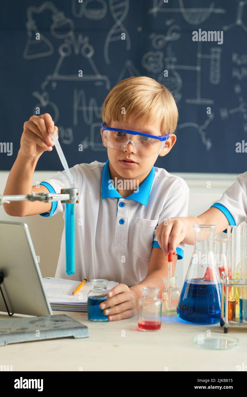 Schoolboy in goggles conducting experiment with chemical liquids Stock ...