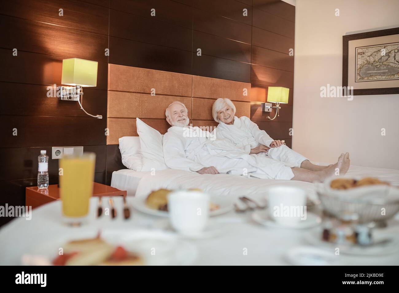 Senior couple in white robes in hotel room before breakfast Stock Photo