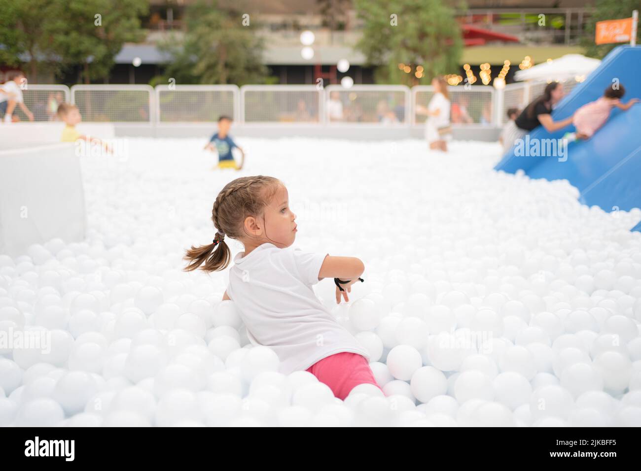 Happy little girl playing white plastic balls pool in amusement park