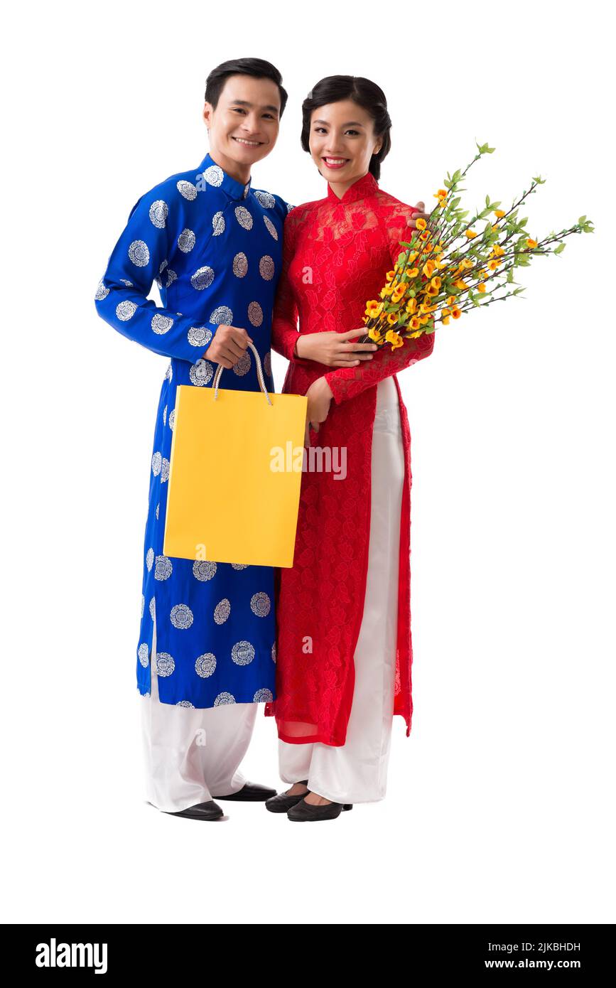 Portrait of happy Asian couple in ao-dai dresses holding apricot tree branches and paper-bags, isolated on white Stock Photo