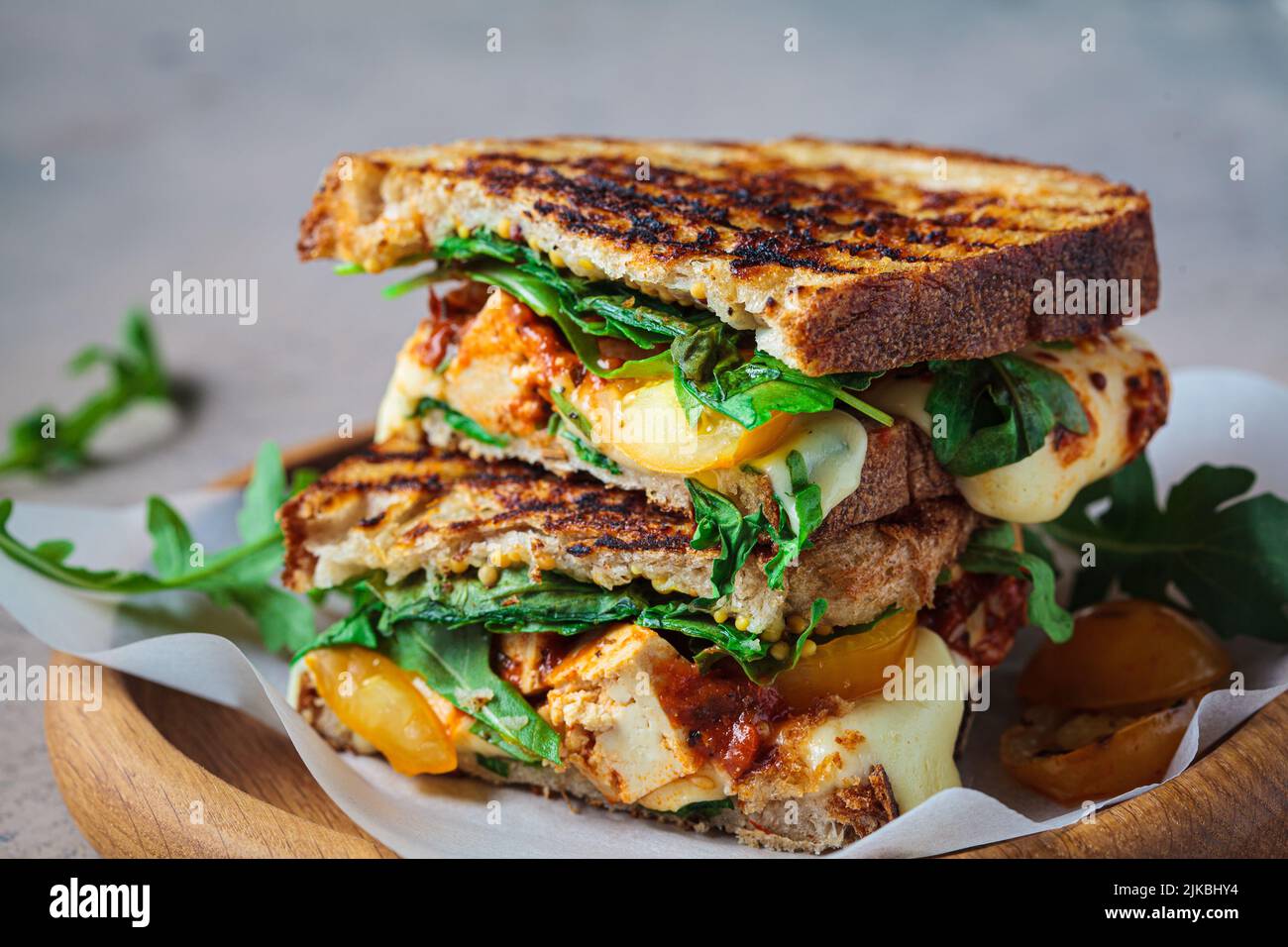 Grilled sandwich with vegetables and mozzarella on a wooden board. Stock Photo