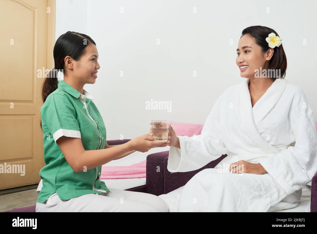 Spa salon administrator offering a glass of fresh water to client Stock