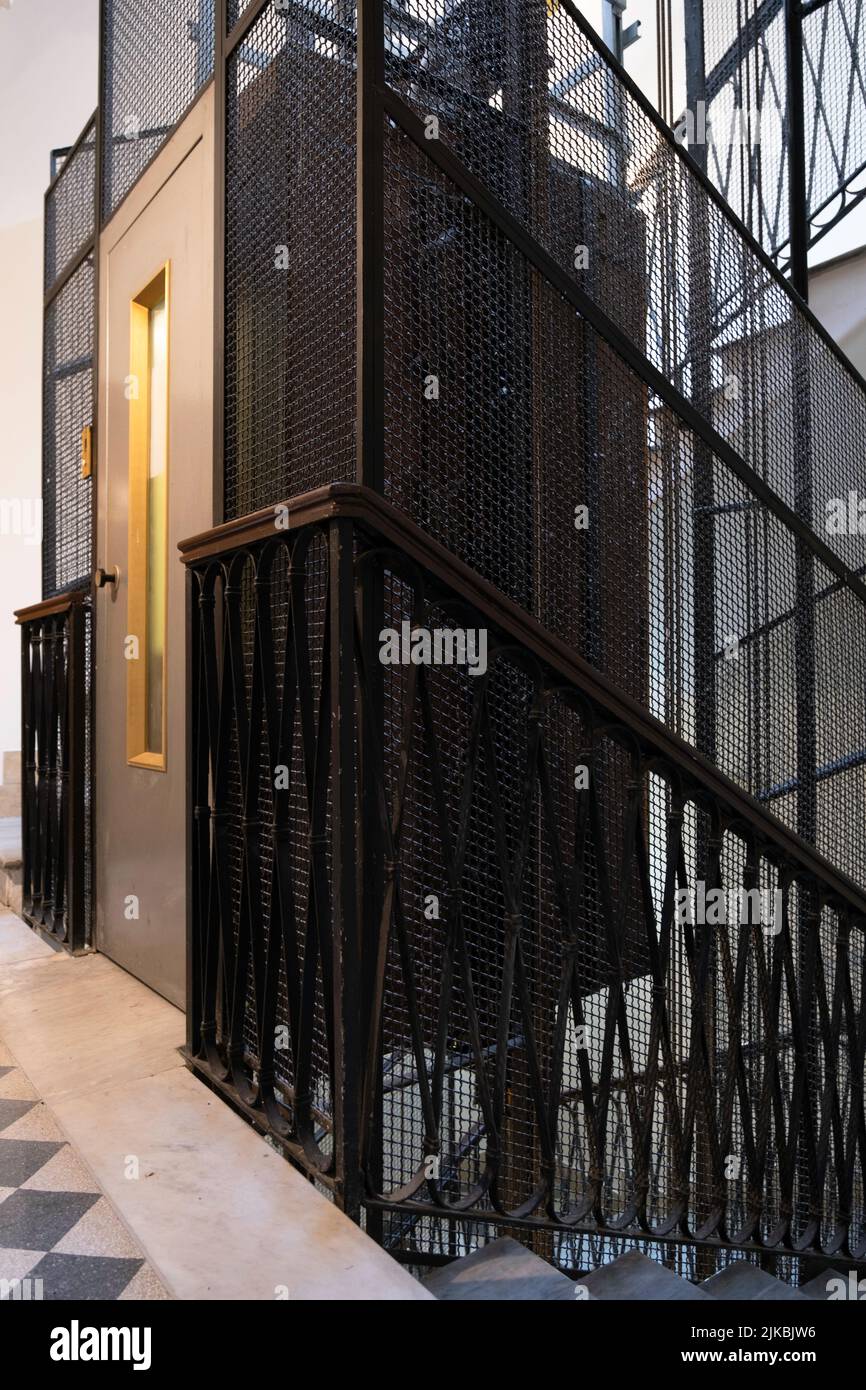 Stairwell with metal frame elevator shaft, wire mesh cage, cables and cabin in a vintage apartment building in Rome, Italy. Narrow depth of field Stock Photo