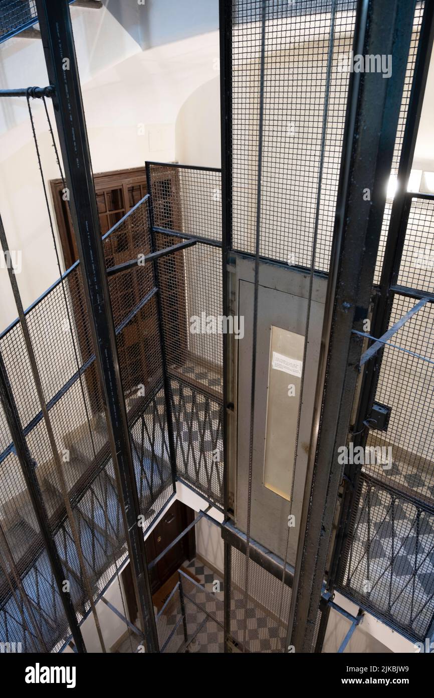 Older elevator shaft with metal frame, fencing, cables and elevator doors in a vintage apartment building. Narrow depth of field Stock Photo