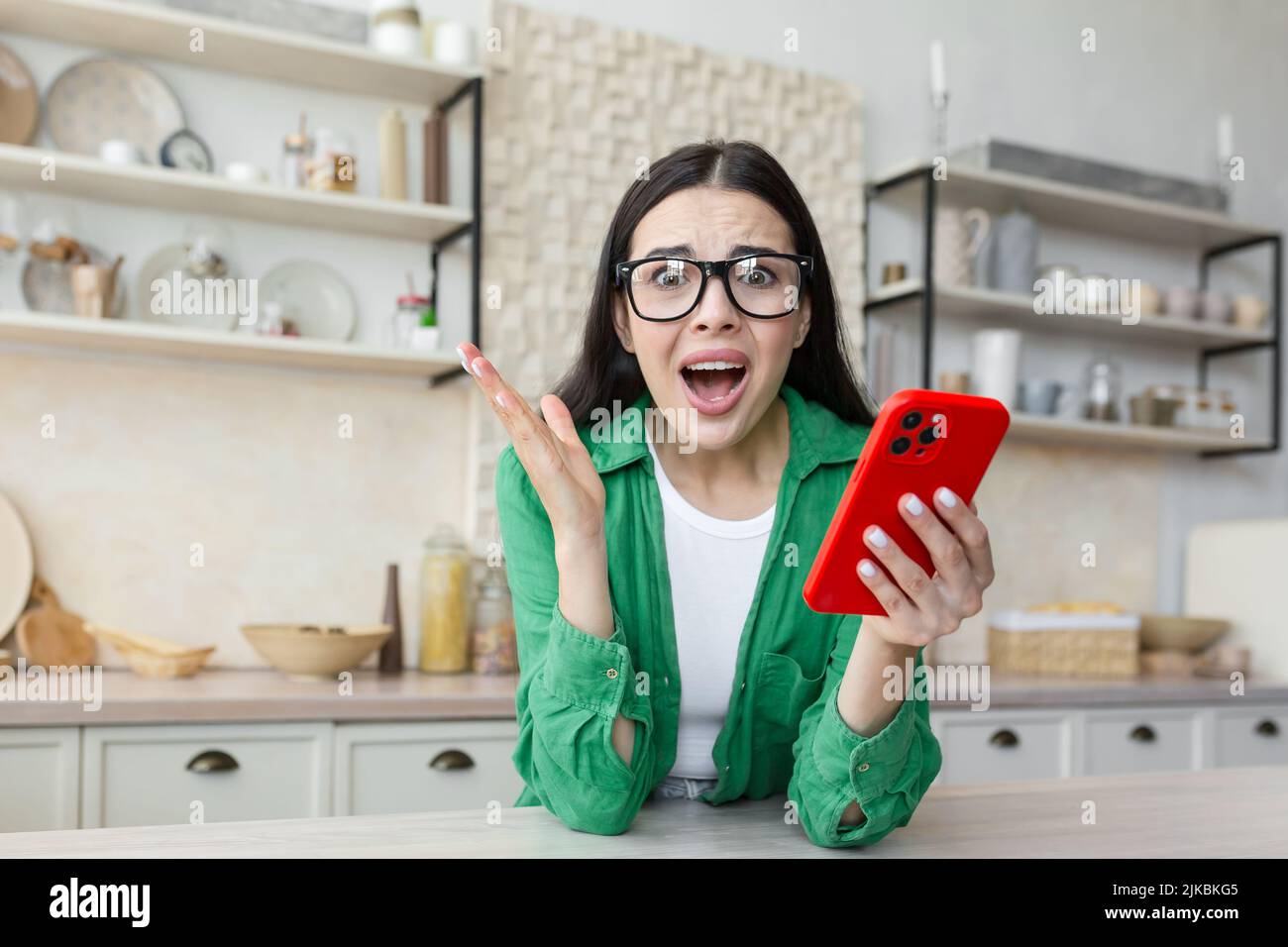 Shocked young woman looking at smartphone screen, feeling confused getting message with unbelievable news. Surprised millennial lady getting unexpected online lottery win notification at home. Stock Photo