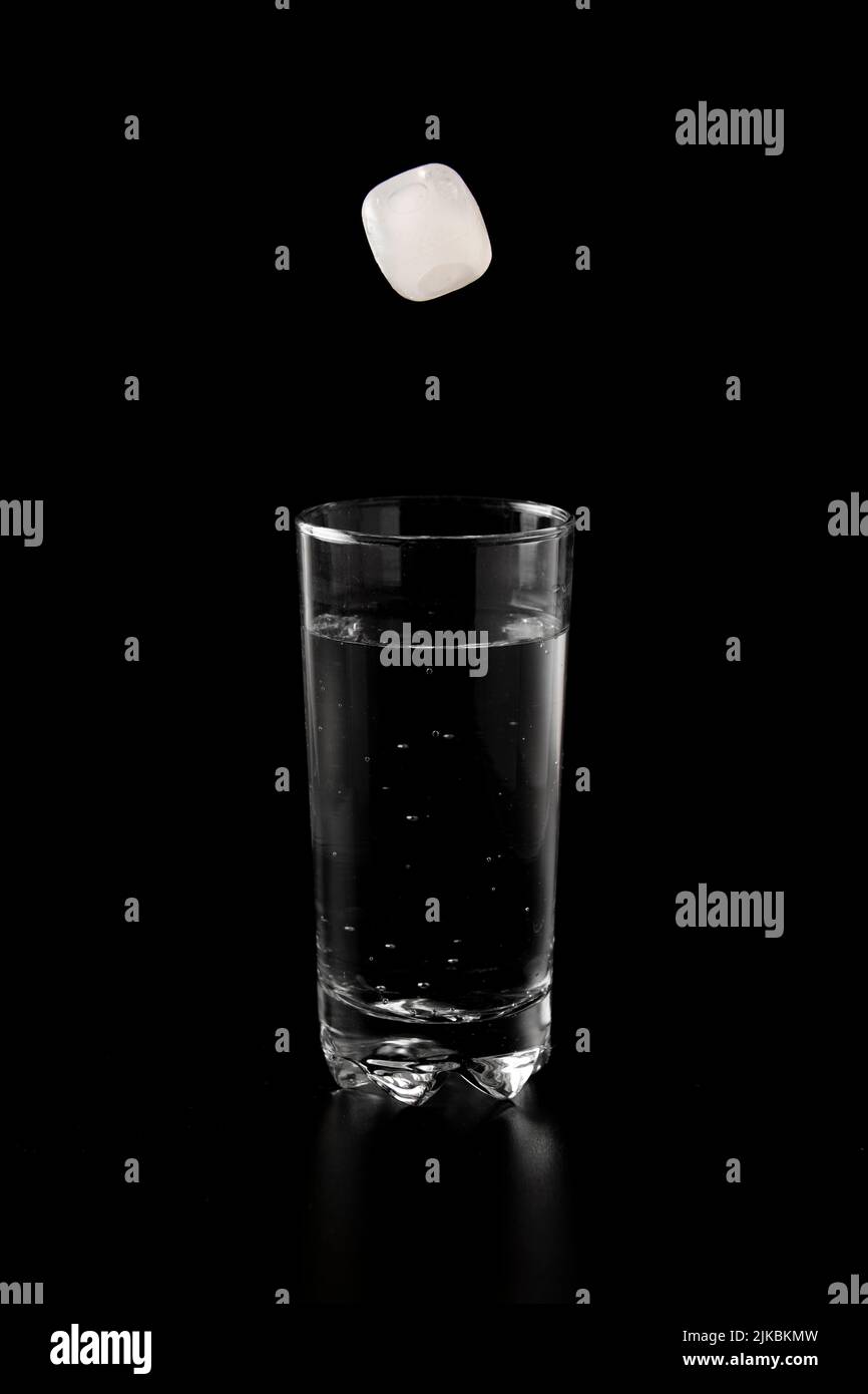 Ice cubes thrown to a glass of water from above with splash on a black ...