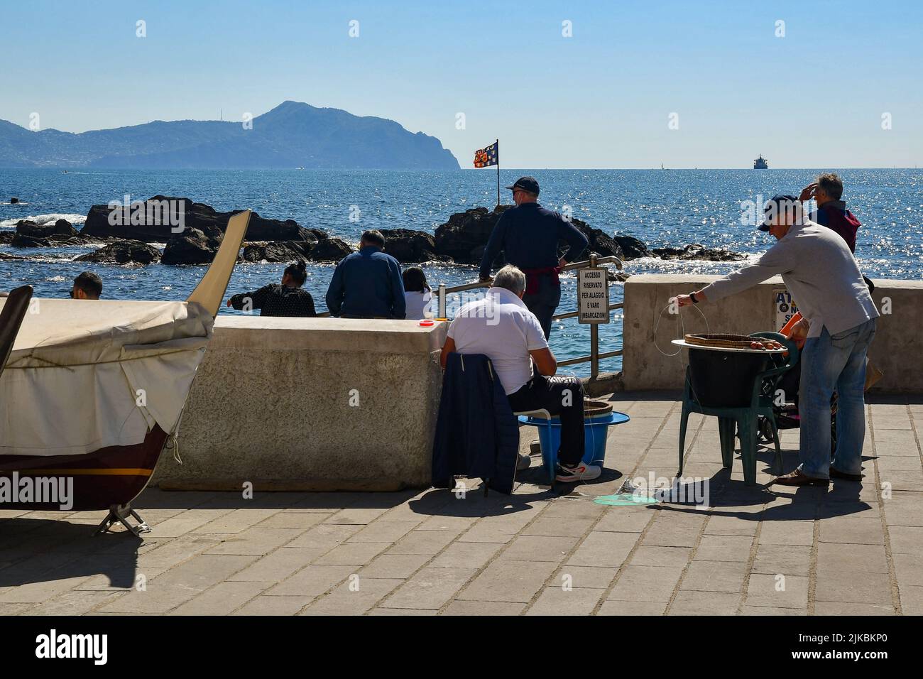 Fishermen repairing fishing nets on the waterfront of the seaside village with the promontory of Portofino in the background, Boccadasse, Genoa Stock Photo