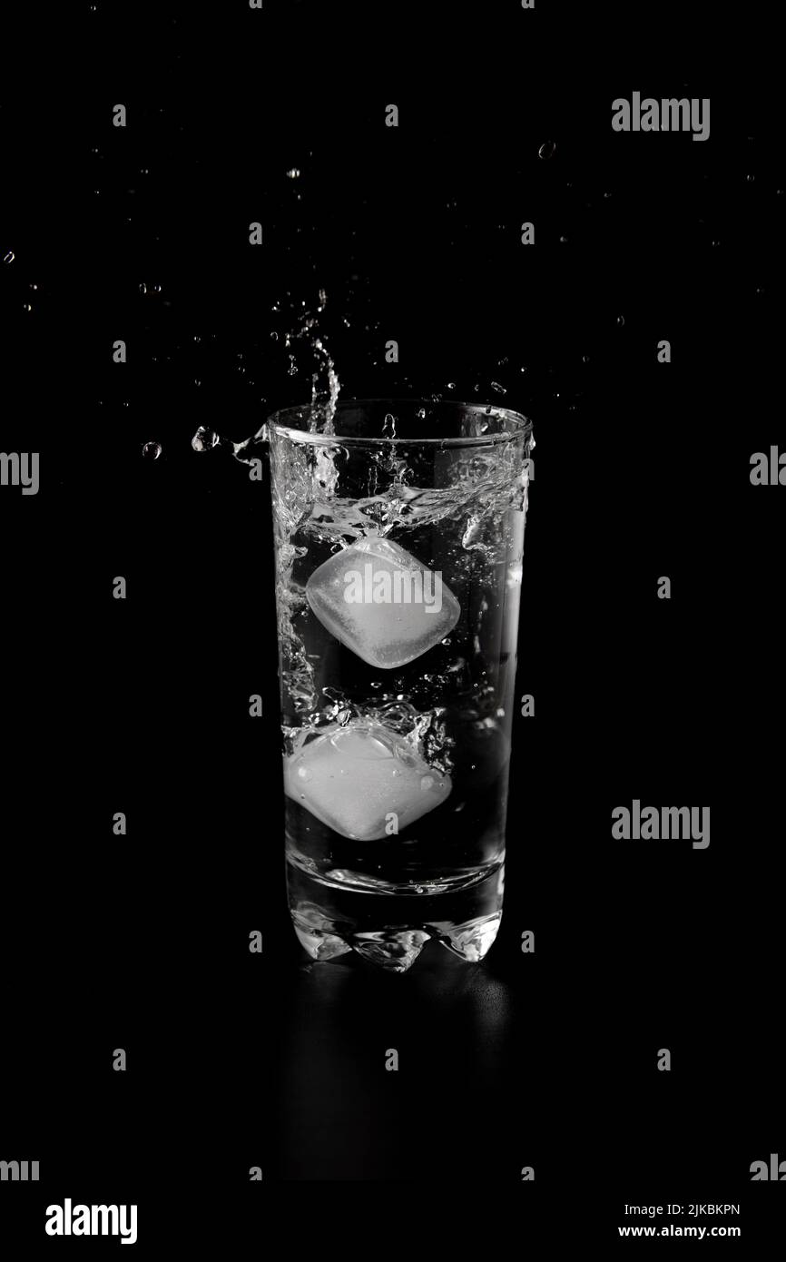 Ice cubes thrown to a glass of water from above with splash on a black ...