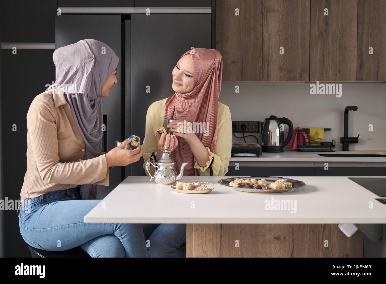 Two muslim women talking, drinking tea and eating arabic sweets. Stock Photo