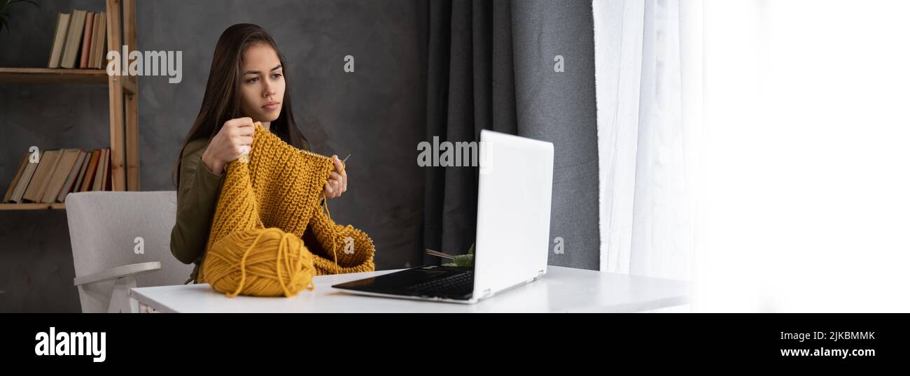 learning to knit online. a young woman knits using a laptop and teaches a lesson for students on knitting with threads on knitting needles Stock Photo