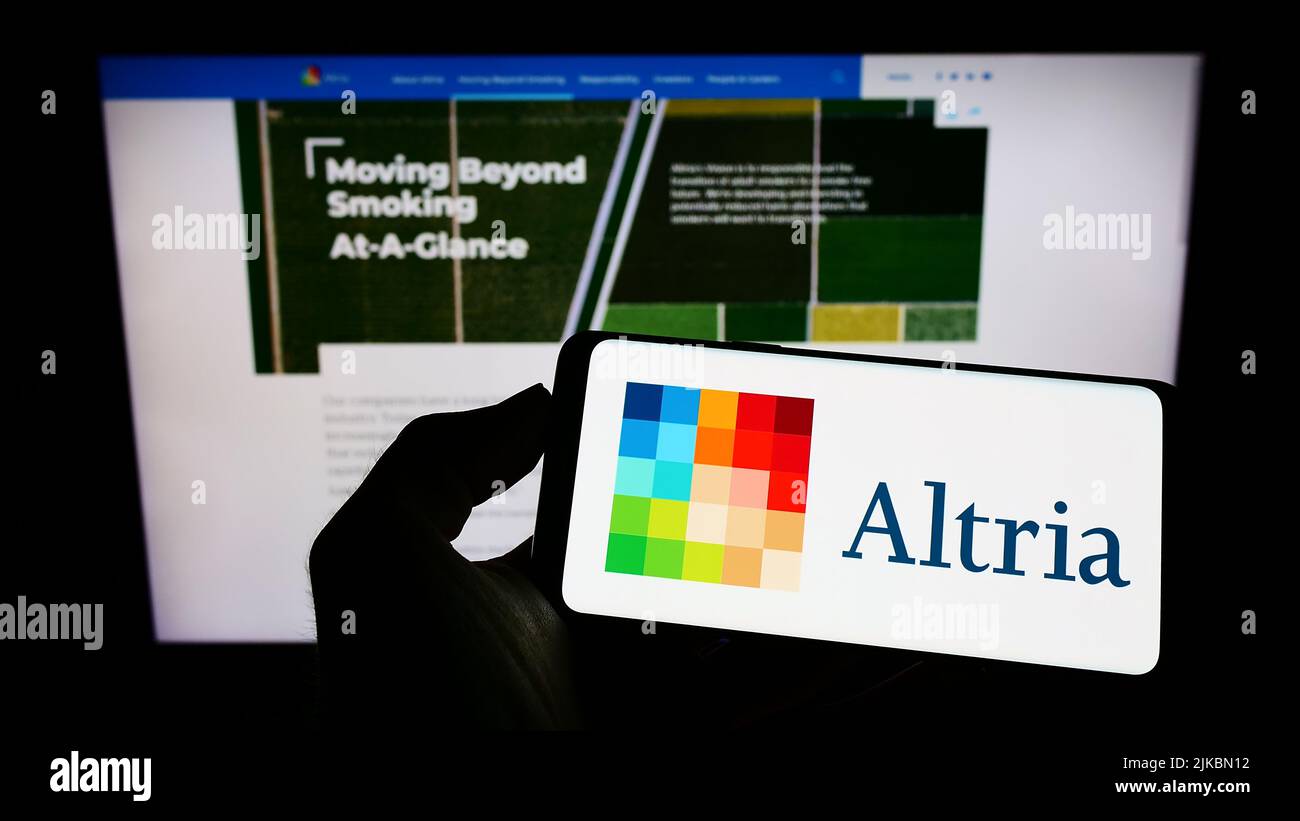 Person holding cellphone with logo of US tobacco company Altria Group Inc. on screen in front of business webpage. Focus on phone display. Stock Photo
