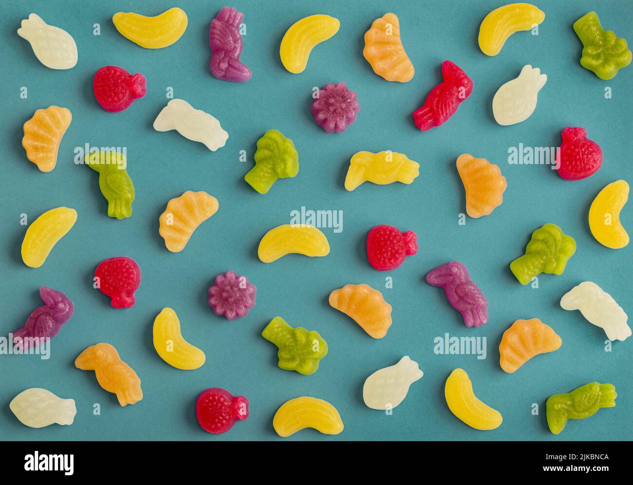 Jelly candies in shape of fruits, trees and birds as pattern on blue