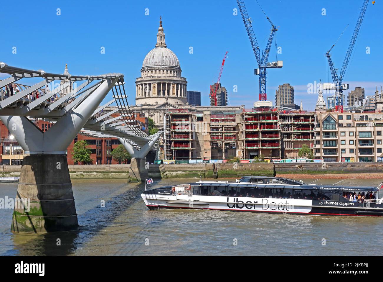 Uber Boat passing under the Millennium bridge, over the Thames, looking over at St Pauls Cathedral and construction cranes, London Stock Photo