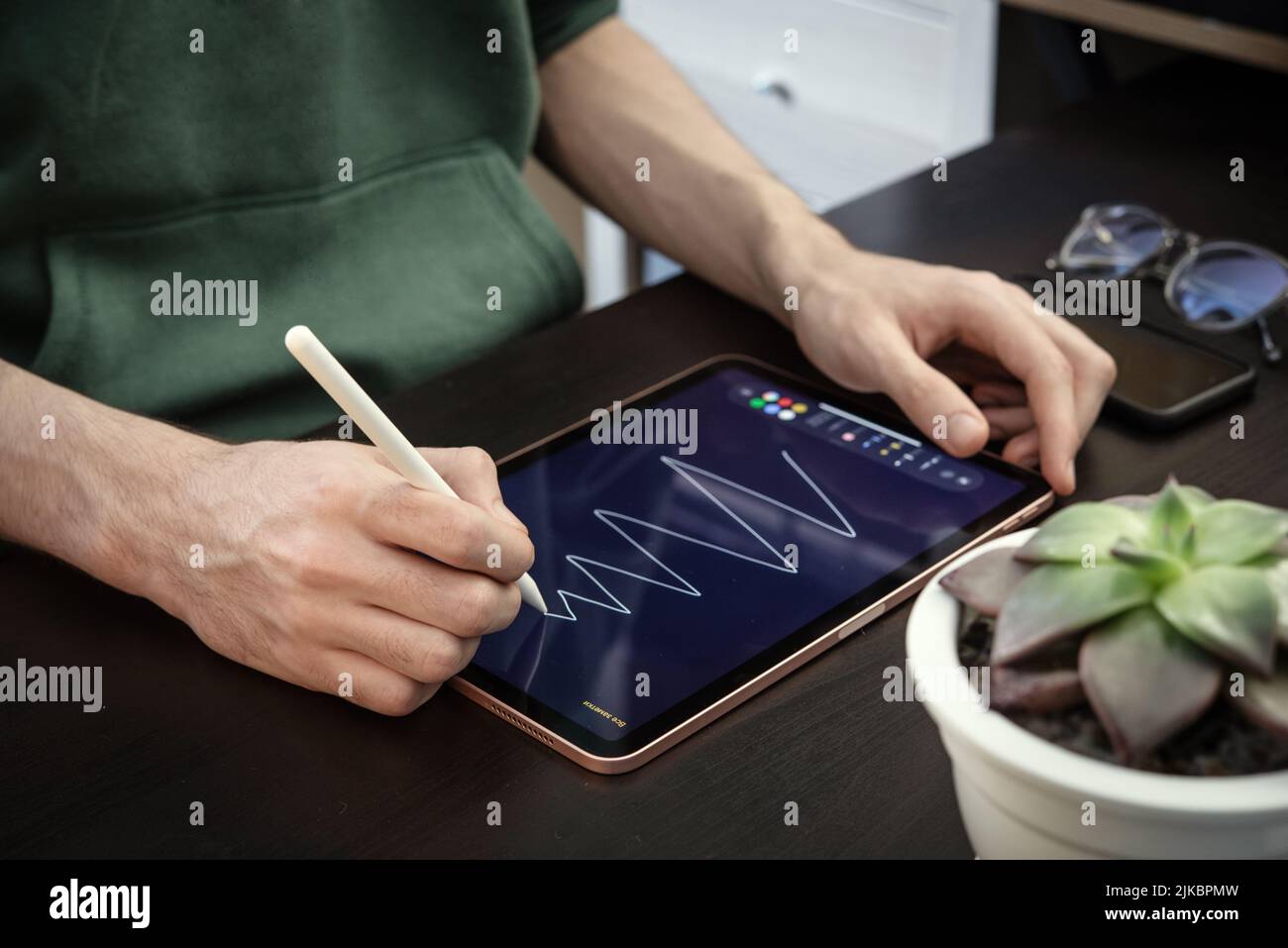 KIEV, UKRAINE - DECEMBER 21, 2021:Man with Apple Pencil using iPad Pro for drawing. iPad Pro was created and developed by the Apple inc. Stock Photo