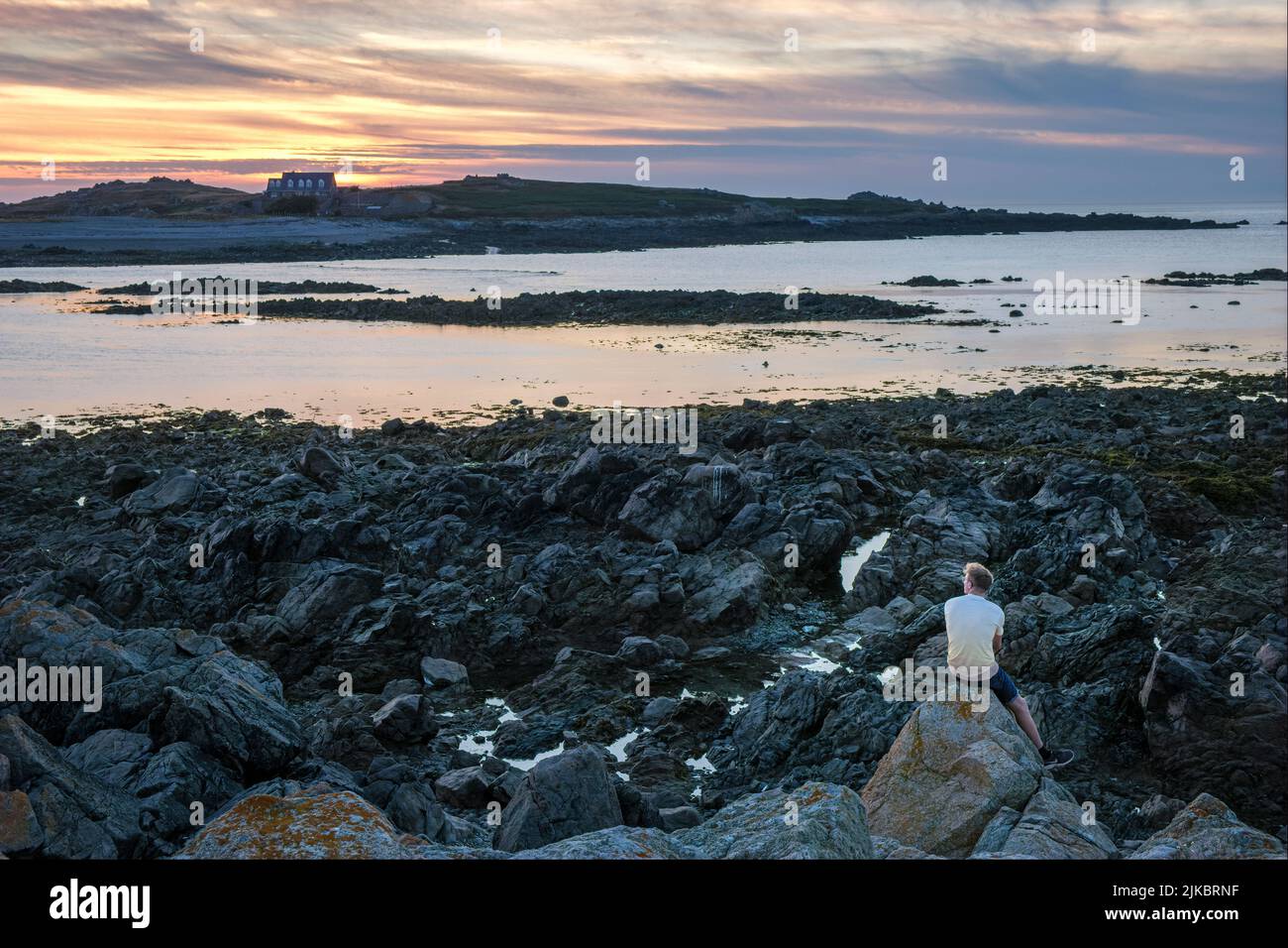 A man watching the sun setting over Lihou Island from L'Erée, Guernsey, Channel Islands Stock Photo