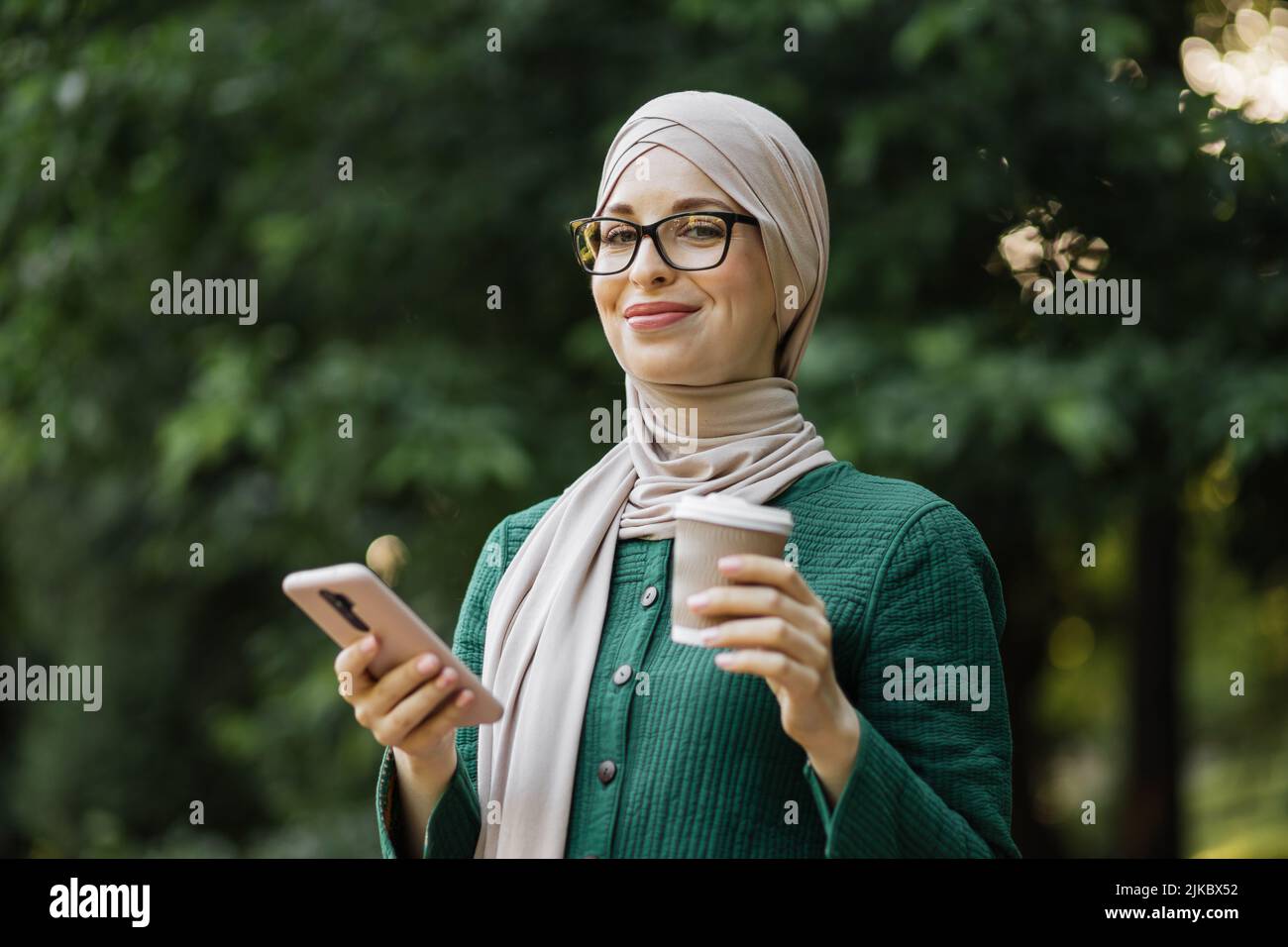Attractive smiling muslim woman in hijab texting on smart phone ...