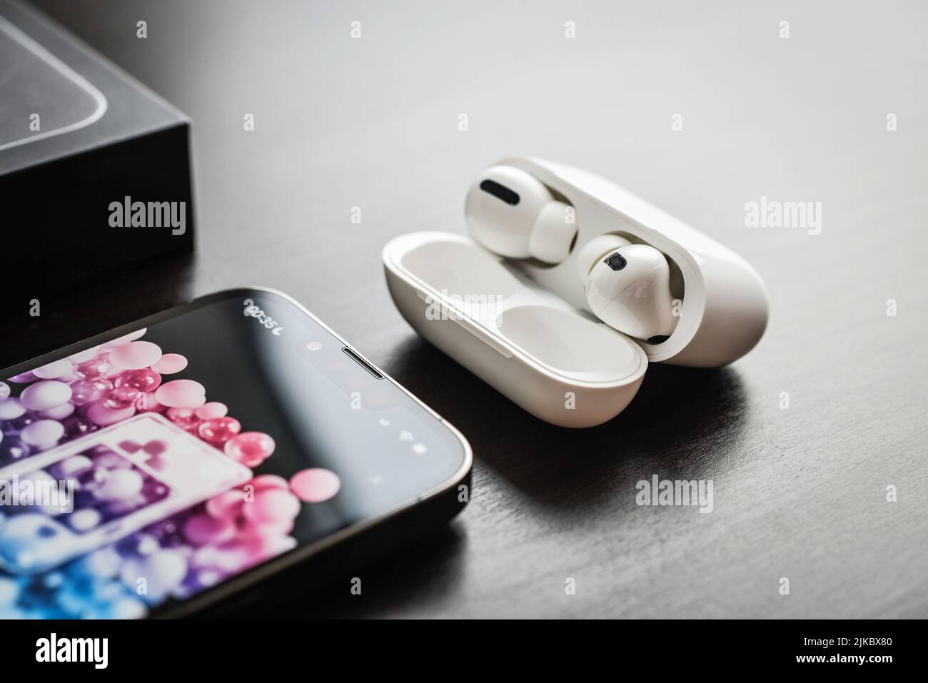 KIEV, UKRAINE - FEBRUARY 10, 2022:  Charging case and the new iPhone 13 Pro with Apple music app on screen next to New Apple Computers AirPods Pro hea Stock Photo
