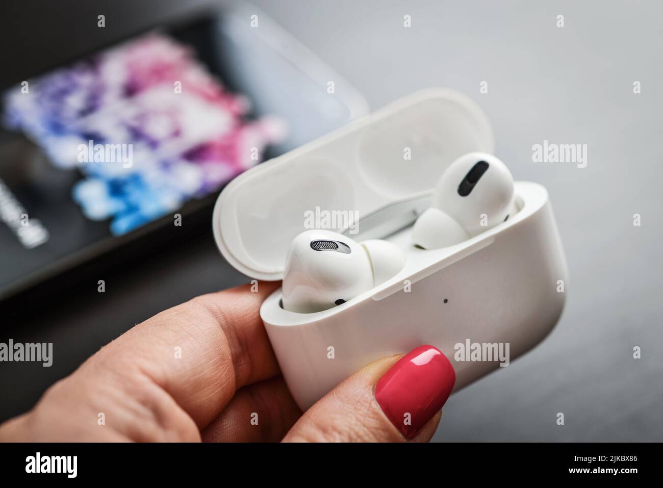KIEV, UKRAINE - FEBRUARY 10, 2022:  Charging case with AirPods Pro headphones  and the new iPhone 13 Pro with Apple music app on screen Stock Photo