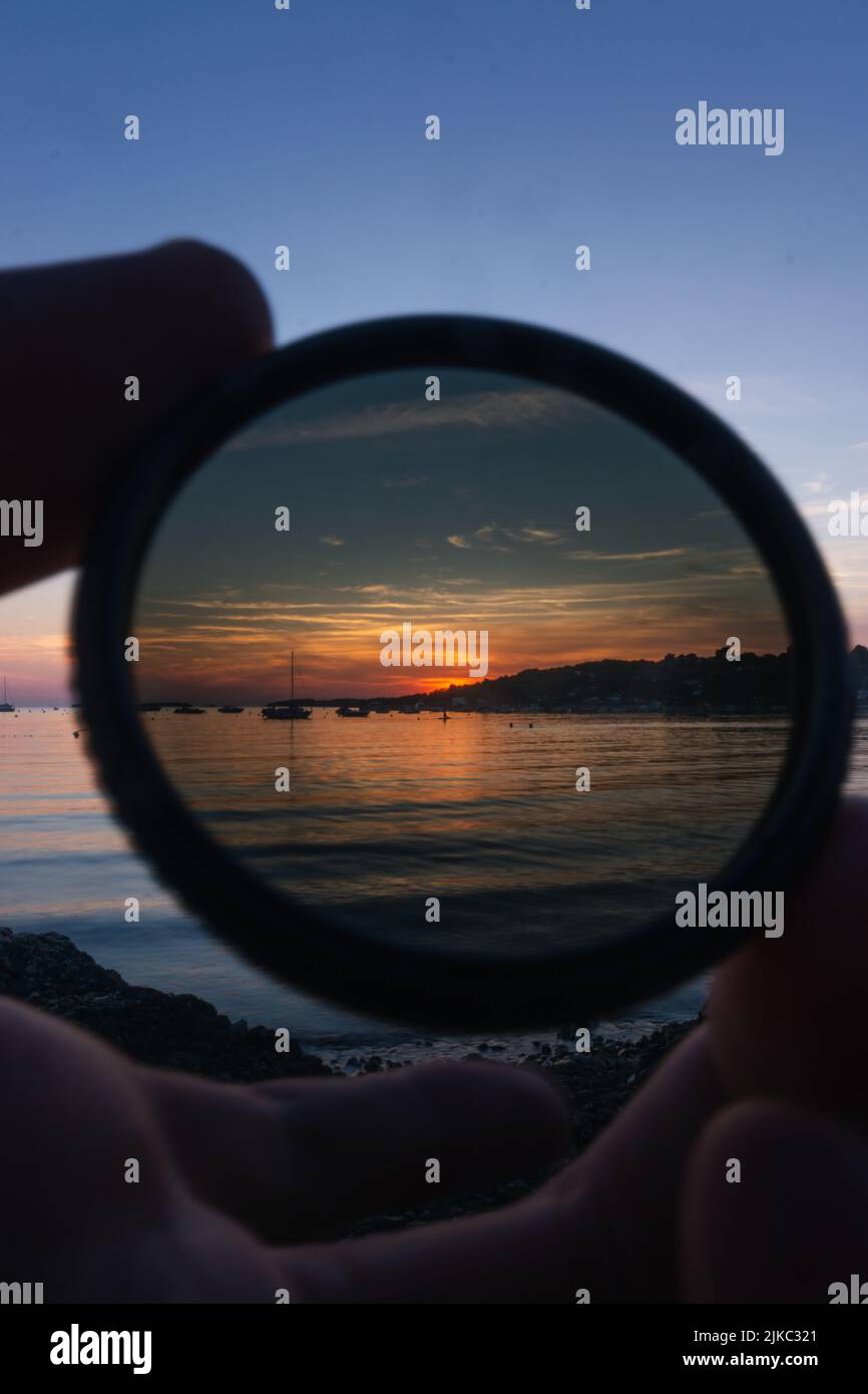 A person holding gradient neutral density ND filter on the background of sea against a scenic sunset Stock Photo