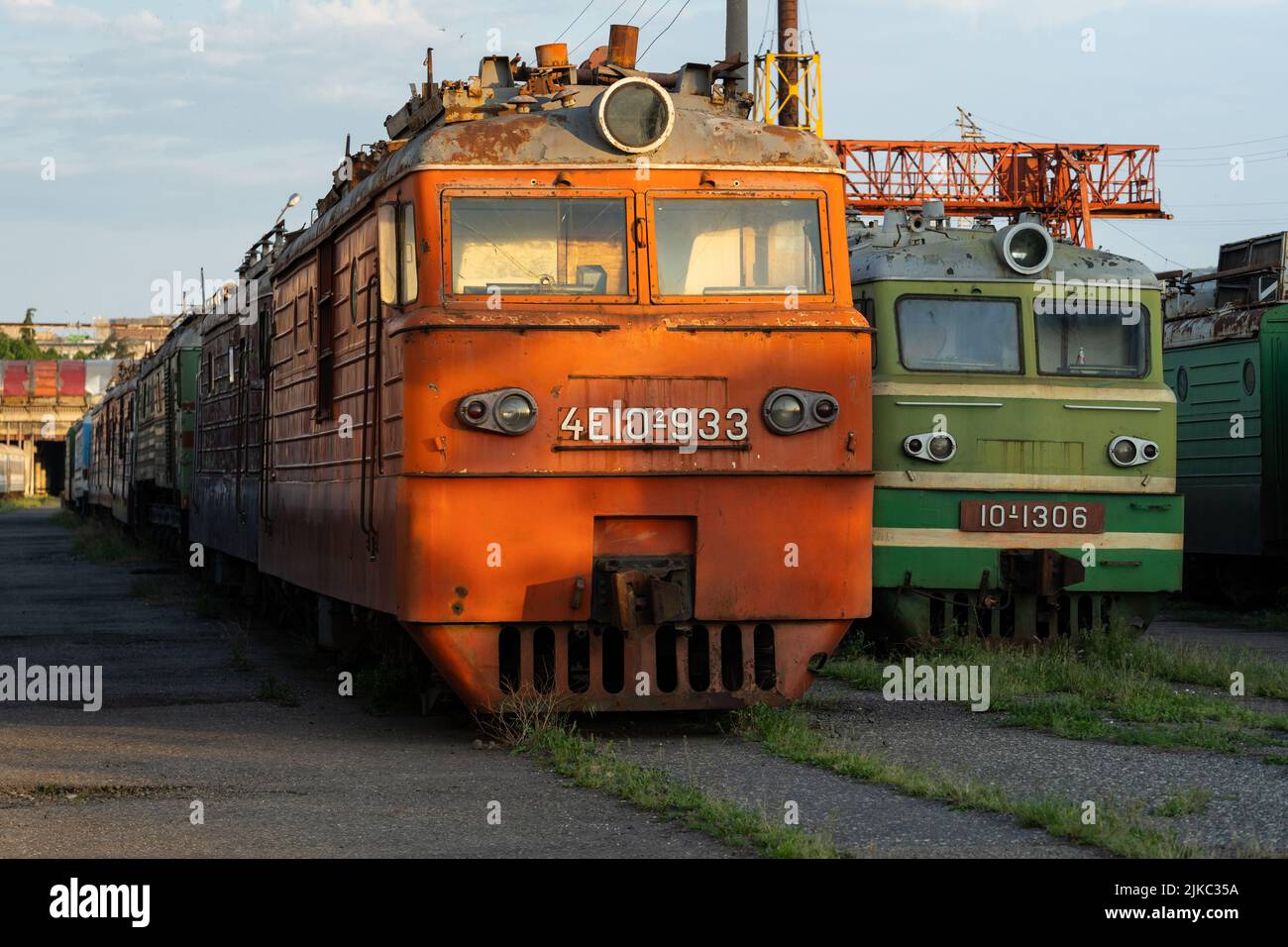 Decommissioned orange and green soviet locomotives stand on overgrown railway in abandoned stock Stock Photo