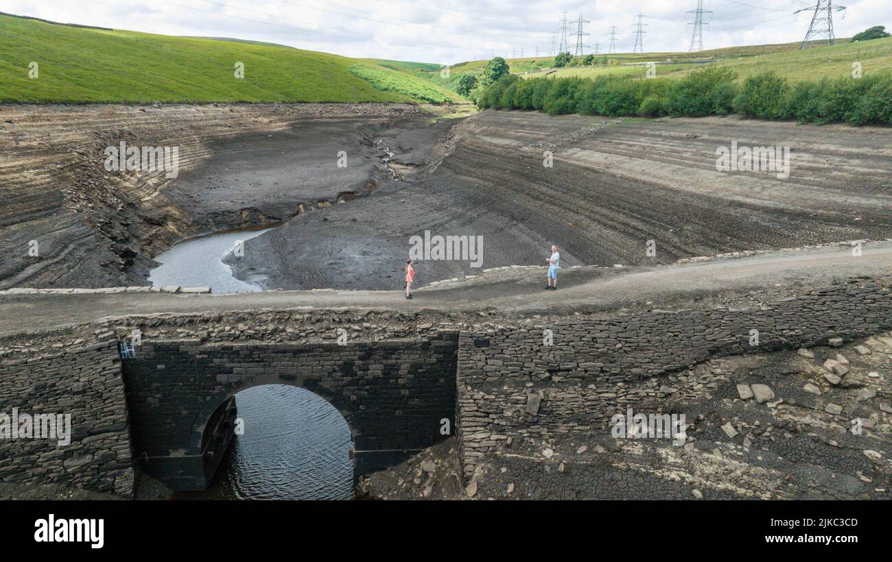 A man and his daughter on an old bridge that’s usual submerged under water is full exposed as water in the reservoir is severally depleted at Baitings Reservoir near Ripponden West Yorkshire, UK on the 01/08/2022 Stock Photo