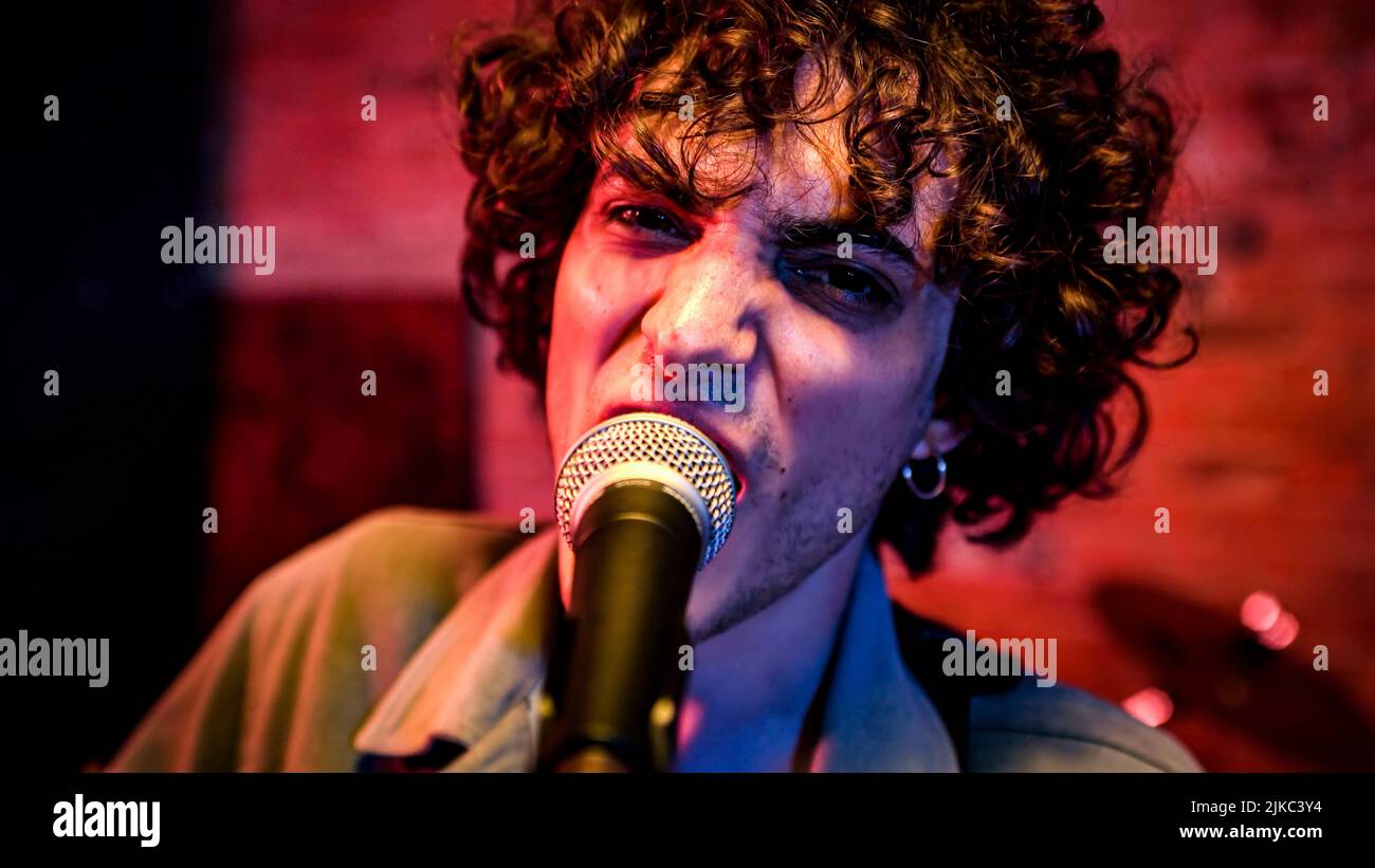 Curly haired rock singer sings a song - Live performance on stage with the band Stock Photo