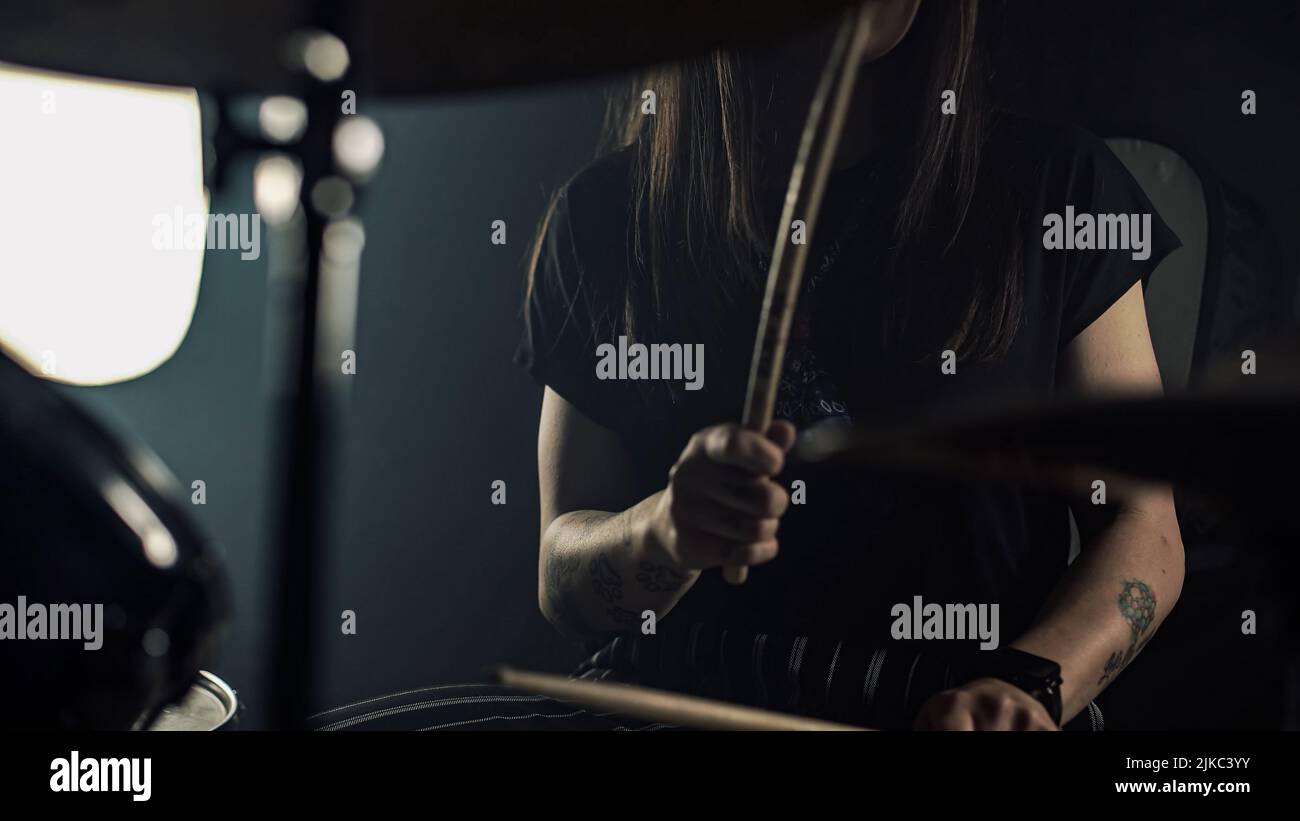 Young female drummer with spectacles plays a drum set holding drumstick in hands Stock Photo